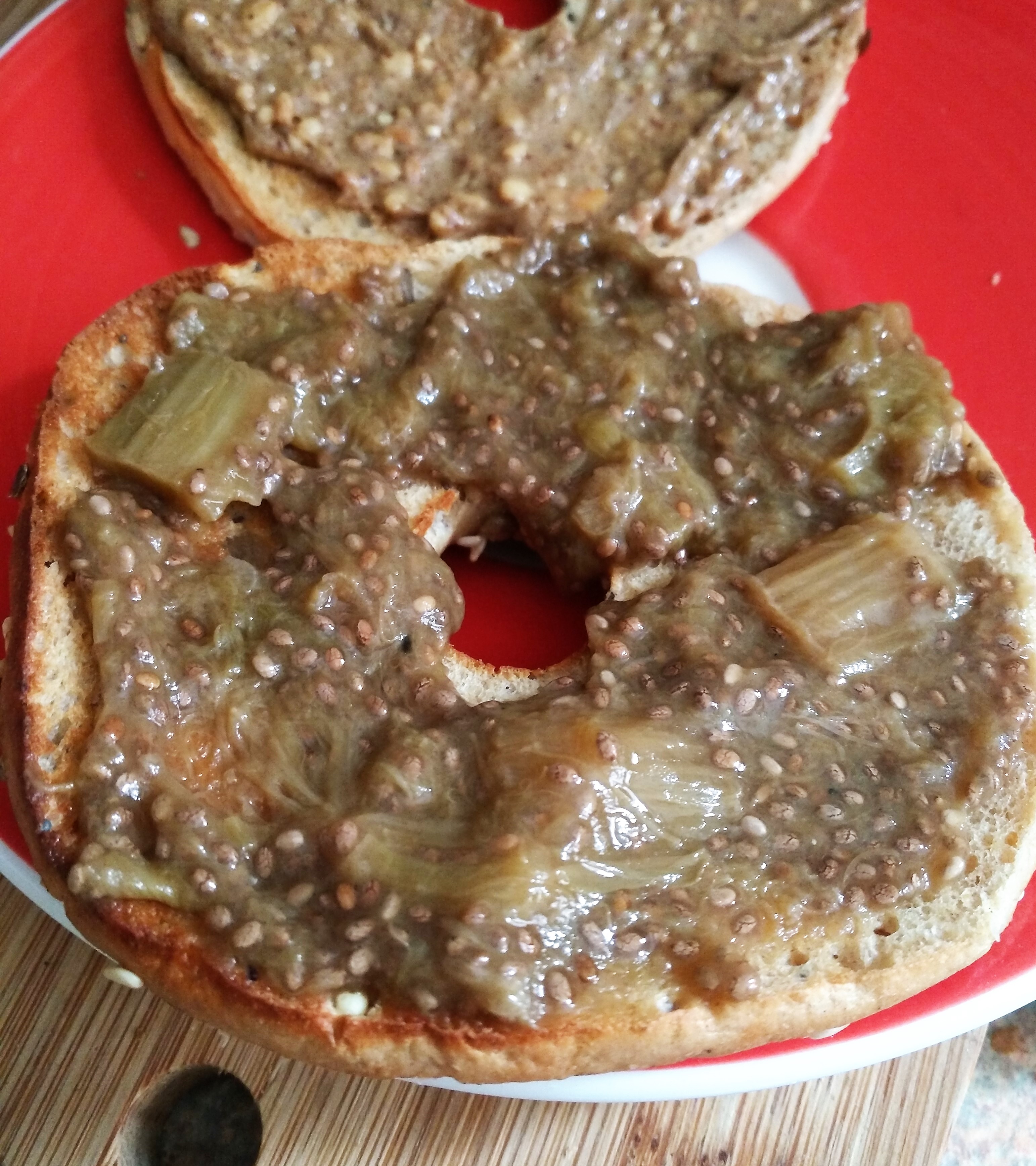 Rhubarb & Ginger Chia jam on a seeded bagel on a red plate on a wooden hedgehog shaped chopping board. Delicious!